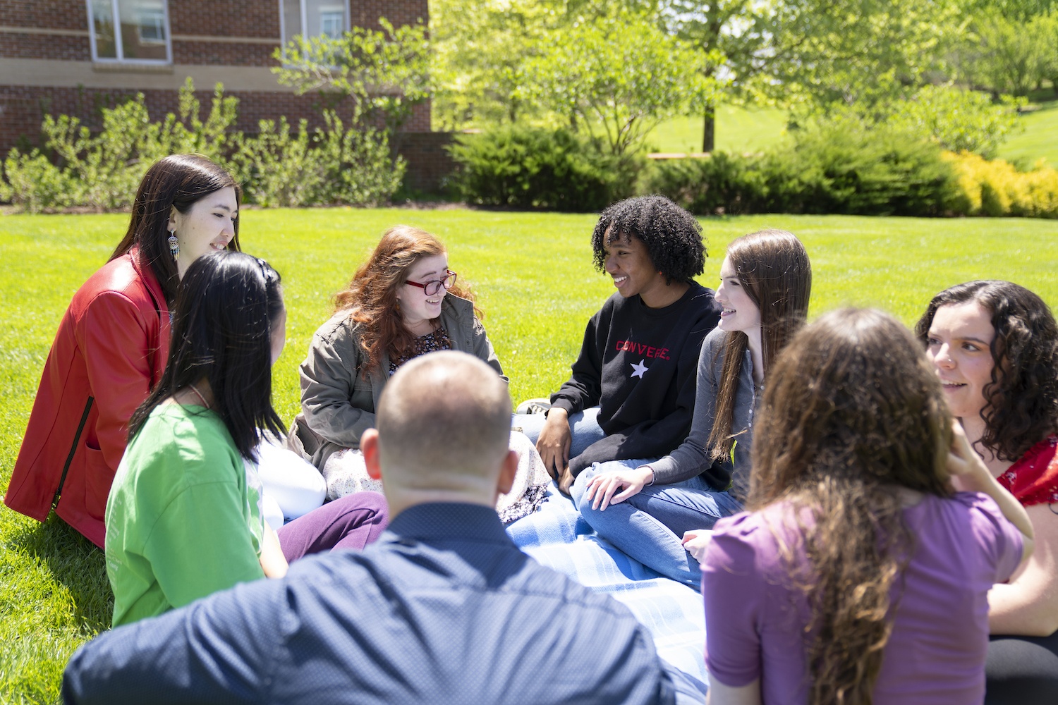 Student sit together outside in the grass.